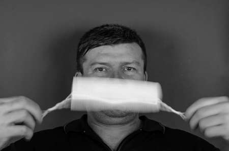 Portrait of an adult male rotating a medical mask in front of his face. A middle-aged man with short graying hair on a gray background. Blurry movement of hands and mask. New normal lifestyleの写真素材
