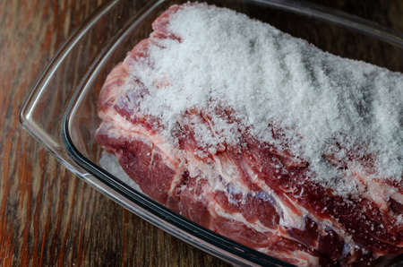 Homemade Capicola (coppa). Dry-cured pork loin step-by-step recipe. Step salting meat. Raw pork meat covered with salt in glass bowl. Traditional Italian cuisine.の写真素材