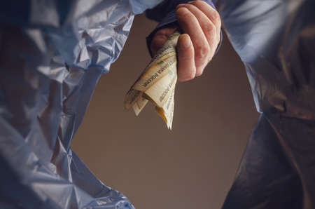The hand throws money in the trash. A man is holding several Russian rubles over the trash garbage can. Inflation, bankruptcy, obsolete money concept. Bottom view.の写真素材