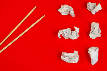 Chopsticks and Crumpled scraps of white paper on a red background. Six pieces of crumpled paper and wooden food sticks. Top view, flat lay.の写真素材
