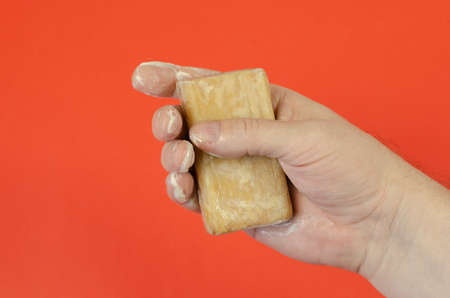 Hand and wet laundry soap on a red background. The man is holding a rectangular bar of brown soap. The palm is covered with soapy foam.の写真素材