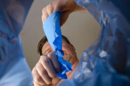 A hand tosses blue medical gloves into a trash can.Man removes protective gloves from hand over garbage basket. View from below. Indoors.の写真素材