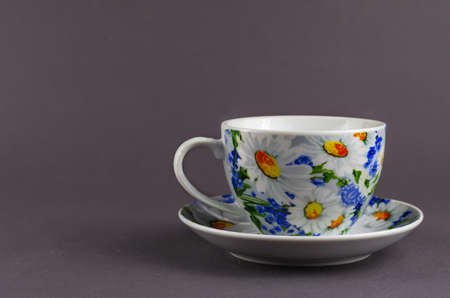 White cup with painted flowers on a gray background. Ceramic Mug cup and saucer for tea or coffee brightly decorated in blue and yellow colors. White daisies on the dishes.の写真素材