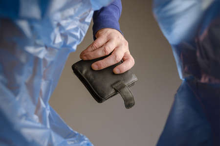 A hand tosses an old black wallet into a trash can. Man holds empty leather purse over garbage basket. View from below. Indoors.の写真素材