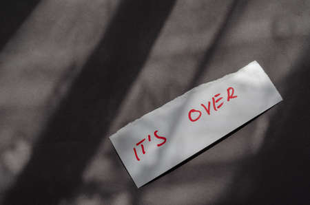 Handwritten note It`s Over on a white piece of paper. A scrap of paper with a jagged edge on a gray background. Top viewの写真素材