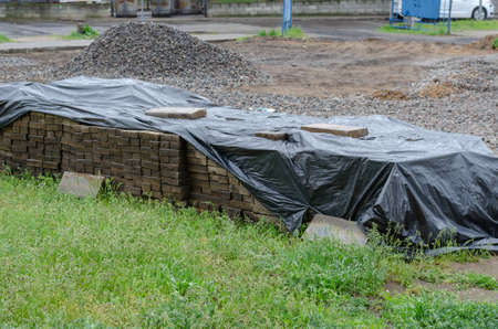 The bricks are covered with black plastic wrap in the foreground. A pile of gray gravel in the background. Construction work, landscaping.の写真素材