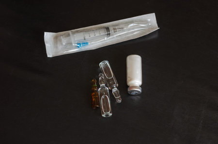A syringe, three ampoules, and a bottle of white powder. Glass ampoules on a black background....