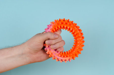A hand clutching a red rubber expansion band against a blue background. Adult male holding a...
