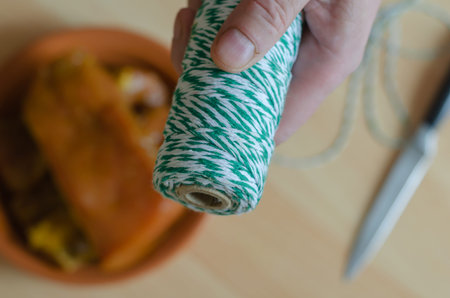 A hand holds a white and green skein of twine over the kitchen table. A clay plate with marinated...