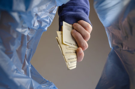 The hand throws money in the trash. A man is holding several Russian rubles over the trash garbage...