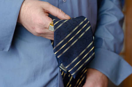 A close-up of a hand holding a blue and yellow striped tie. A middle-aged man with a gold ring on his index finger. Lifestyle. Indoor.の写真素材