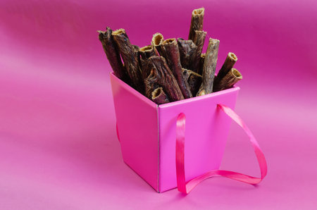 Gift Box of pet treats on a pink background. Dried dog goodies. Delicious Red Beef Gullet Sticks. Bovine esophagus.の写真素材