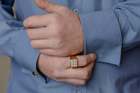 Close-up of hands buttoning a cufflink on the sleeve of a blue shirt. A middle-aged adult man with a...