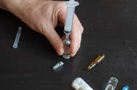 A hand, three ampoules, and a bottle of white powder. The hand fills the syringe with medicine from the ampoule. Close-up, selective focus.の写真素材
