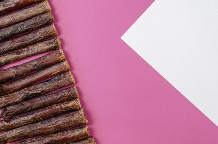 Sticks of dog treats and a blank white sheet on a pink background. Dried beef esophagus. Natural chewy goodies for pets.の写真素材