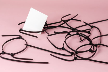 Black wire ties and white abstract geometric shapes on a pink background. Old cut plastic ties...