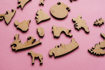 Wooden puzzle on a pink background. Puzzle pieces in the shape of animals and other complex shapes....