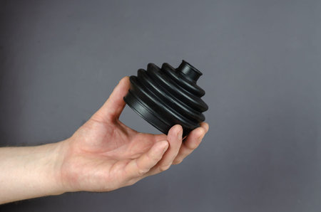A man is hold Black rubber drive shaft cover against a gray background. New Drive shaft boot. Spare...
