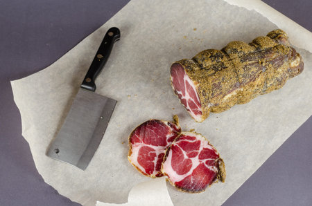 Cured meat, pork neck, coppa. A piece of appetizing air-dried pork on parchment. Ready-to-eat food....