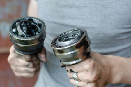 A young adult holds a new and old Drive shaft joint in his hand. A man with silver rings on his fingers holding car parts. Auto Service.の写真素材