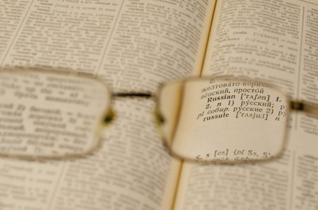 Reading glasses and an open book in close-up. Old Russian-English Dictionary. Selective Focus on the...