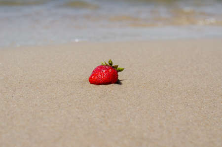 A ripe red strawberry on the wet yellow sand. The strawberry lies on the beach, washed by the wave. Selective focus.の写真素材