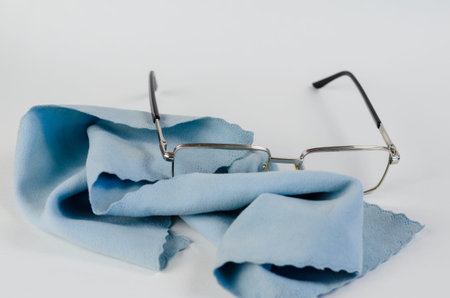 Reading glasses and a napkin on a white background. Metal-rimmed glasses and a blue special cleaning...