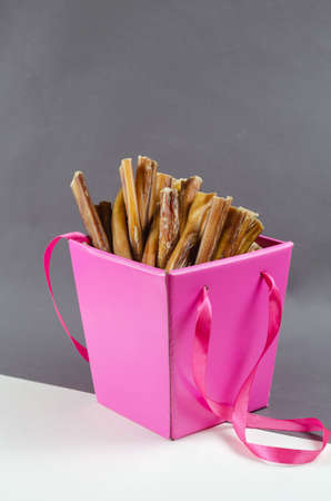 Pretty pink gift box with pet treats. Open box full of bully sticks for dogs on gray and white background. Chewing treats. Beef pizzle.の写真素材