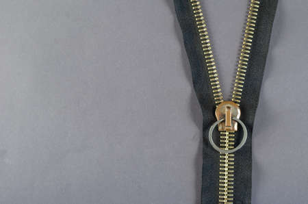 Metal zipper on gray background. Clasp with yellow prongs and black braid. Copy space. Top view.の写真素材