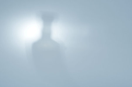 Bottle in the Light. Blurred silhouette of a whiskey bottle on blue. Defocused shadow with noise....