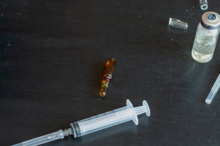 A syringe, three ampoules, and a bottle of white powder. Glass ampoules on a black background....