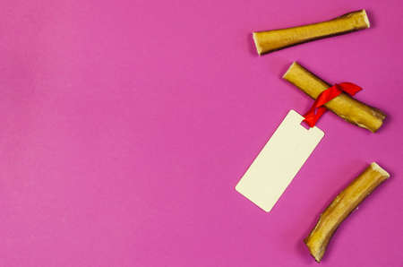 Dog treats and sales tag on pink background. Air dried pet sticks. Bully sticks. Beef pizzle. Tag is tied with red ribbon. Top view. Copy space.の写真素材