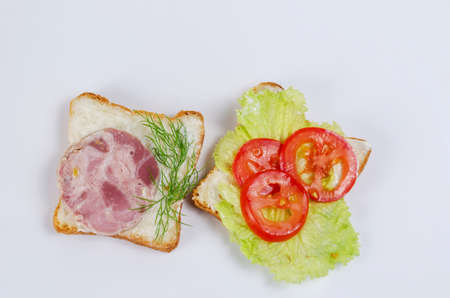 Sandwiches on a white background. Two sandwiches with ham, red tomatoes, green lettuce, dill and cream sauce. Top view.の写真素材