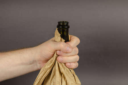 Social problem of alcoholism concept. Shaking hand holds an open Bottle of Alcohol in paper bag. Dark bottle in crumpled brown bag. Close-up. Selective focus.の写真素材
