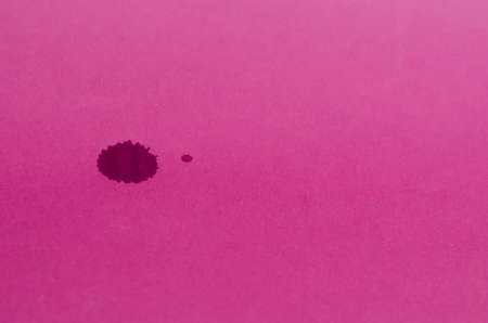 Minimalist composition with dark spots on a pink background. Two spilled drops of red wine on colored paper. A large and a small stain. Selective focus. No people.の写真素材