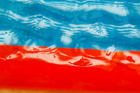 Defocused shot of transparent water against blue and red. Water surface swimming pool with waves and ripples. Freshwater texture. Indoors. Top view. Motion blur, selective focus, noise effectの写真素材