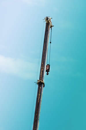Raised boom of 100-ton mobile crane against the sky. Extended telescopic section of cargo crane with hook. Commercial vehicles. Industry.の写真素材