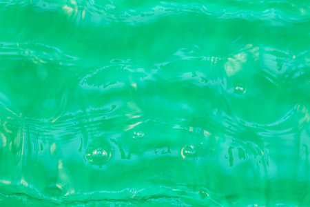 Defocused shot stream of transparent water against green. Irregular surface of fast-flowing stream....