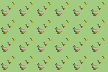 Repeated Children toy figurine of goose on a colored background. Alternating Plastic poultry against pastel greenの写真素材