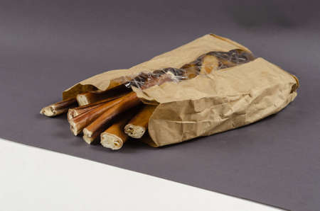Pet treats in a paper bag with transparent window. Dental treats on gray and white background. Bully sticks. Beef pizzle for dog. Natural air dried chewing sticks. Angled top viewの写真素材