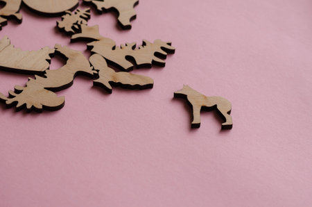 Wooden puzzle on a pink background. Puzzle pieces in the shape of animals and other complex shapes....