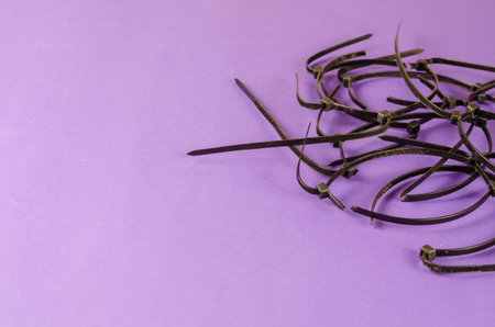Black wire ties on lilac background. Old cut plastic ties randomly on colored background. Angled...