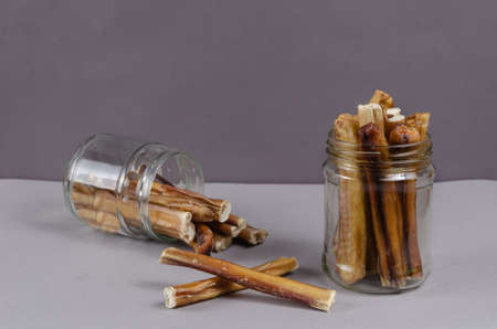 Pet treats in a glass jar on a gray background. Dried bully sticks for dogs. Beef pizzle. Air-dried chew treats.の写真素材