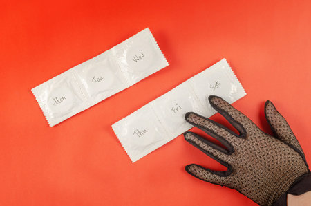 A woman's hand in a black lace glove and condoms on a red background. Days of the week are written...