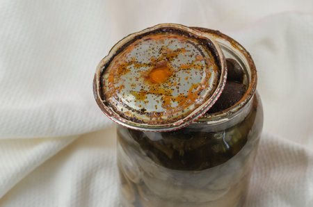 Opened Glass jar with homemade pickled mushrooms. Rusty tin lid with black spots. Spoiled blackened...