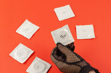 A woman's hand in a black lace glove and condoms on a red background. Days of the week are written...
