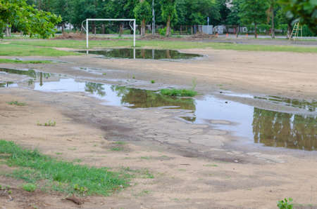 A soccer field with puddles after a downpour. An empty sports field with a white goalpost. Daytime. No people.の写真素材