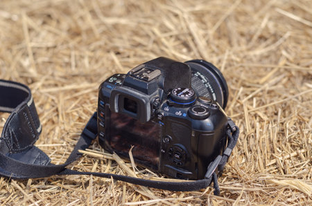 A black digital SLR camera lies on dry yellow hay. Summertime, daytime, no people. Kherson, Ukraine - 08 10 2021.のeditorial素材