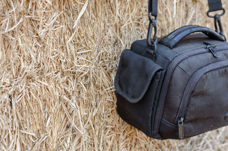 Close-up Black camera bag hanging against a wall of dry straw. A small waterproof camera bag. Warehouse of rectangular bales of hay.の写真素材