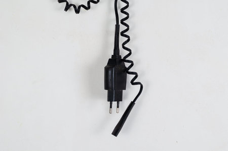A black electrical cord with spiral wire hangs against the white wall. A charger for an electric...